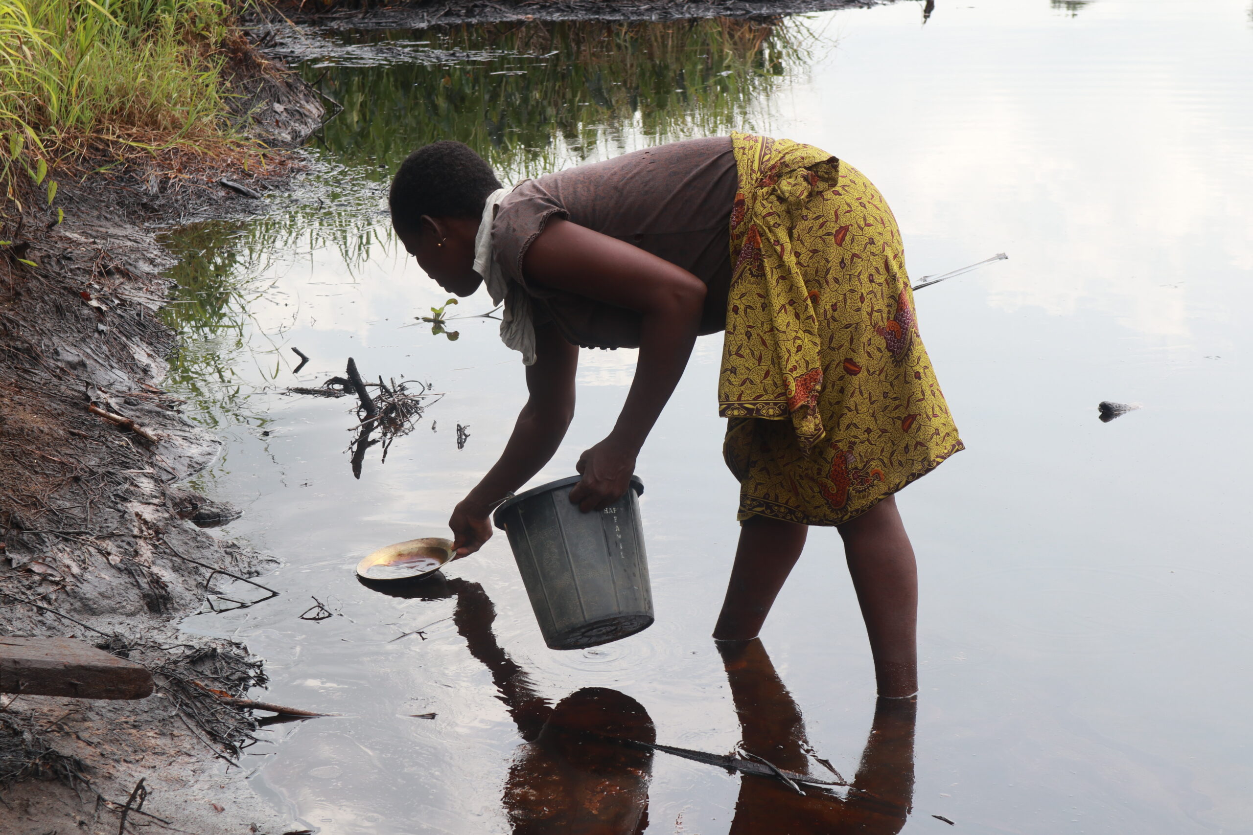Community member in Omoviri attempting cleanup by manually scooping crude oil from the surface of the water